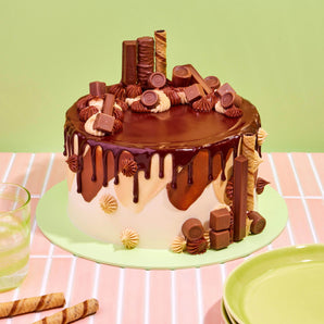 Tuck Shop Cake decorated with chocolate ganache drip and topped with Rolos, Twix, Kit-Kats, and Munchies chocolates.